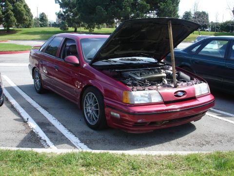 1993 Ford Taurus - A red sedan, identified as a 1993 Ford Taurus, is parked with its hood open, revealing the engine compartment.