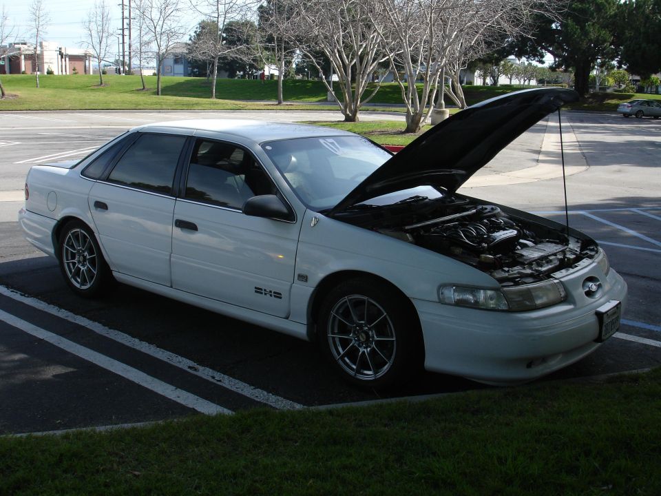 White sedan, hood open, showing engine. Aftermarket wheels. Parked in a lot