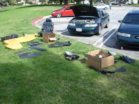 1993 Ford Taurus - A green 1993 Ford Taurus is parked with its hood open, surrounded by interior and exterior parts laid out on the grass.