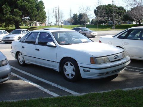 1993 Ford Taurus - A white sedan is parked in a lot with other vehicles visible.
