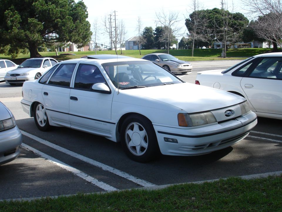 White sedan parked in a lot. It has a sunroof and a body kit