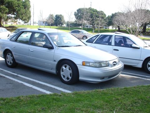 1993 Ford Taurus - A silver sedan is parked next to a white sedan in an outdoor lot.