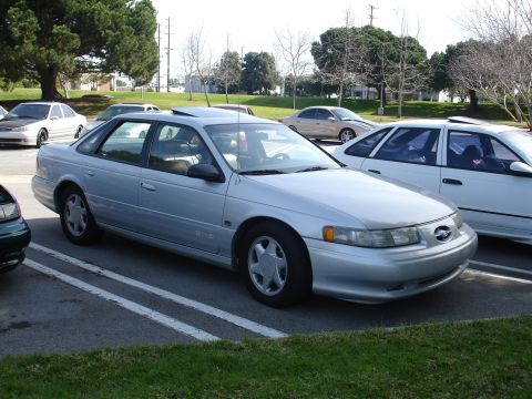 1993 Ford Taurus - A silver 1993 Ford Taurus sedan is seen parked in a lot with other vehicles.