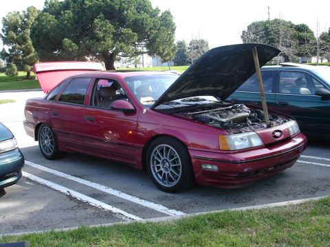 1993 Ford Taurus - Red 1993 Ford Taurus sedan with hood propped open, parked next to another vehicle.