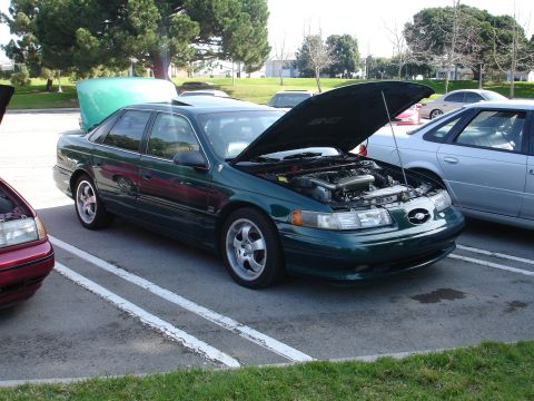 1993 Ford Taurus - A green sedan is parked with its hood open, revealing the engine compartment. Other vehicles are visible in the background.