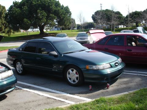 1993 Ford Taurus - A green sedan with a sunroof is parked in a lot next to other vehicles.