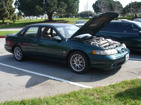 1993 Ford Taurus - A green 1993 Ford Taurus sedan is parked with its hood open, revealing the engine bay.