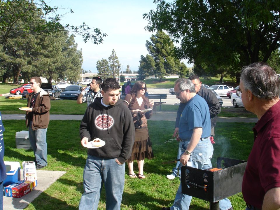 People gathered in a park for a picnic, with cars parked in the background
