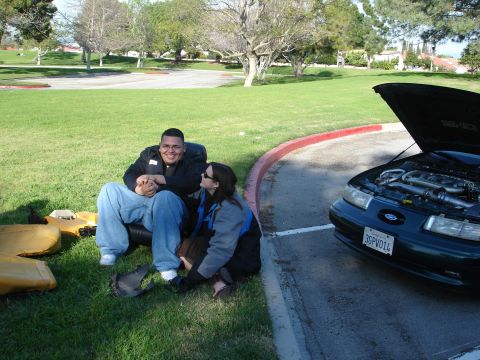 1993 Ford Taurus - A dark green sedan with its hood open is parked next to a curb, with two people sitting on the grass.