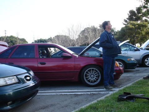 1993 Ford Taurus - Several cars are parked in a lot, with a man standing beside a maroon sedan.