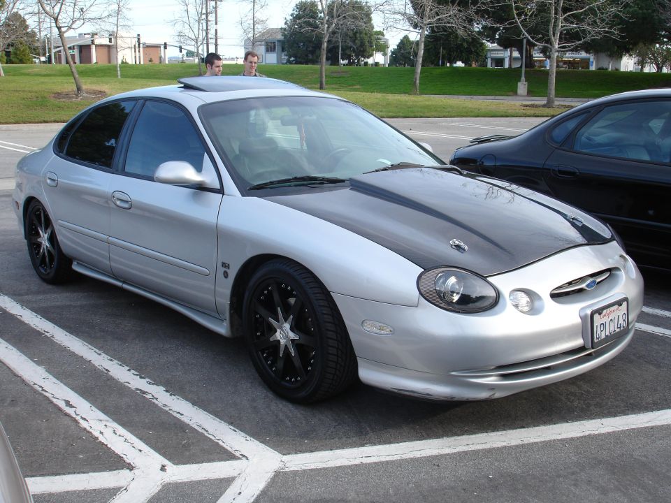 Silver sedan with a black hood and custom rims parked in a lot. Another black car is next to it