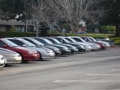 1993 Ford Taurus - A line of sedans, including a red one and several silver ones, are parked in an outdoor lot.
