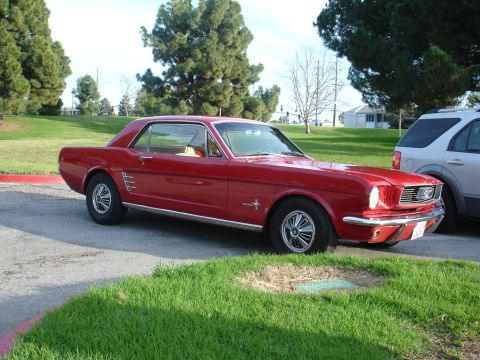 1993 Ford Taurus - A classic red Ford Mustang is parked on the side of the road next to a modern SUV.