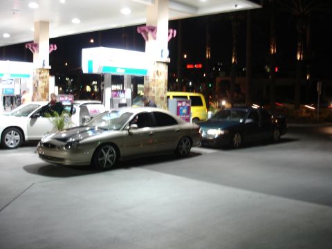 1993 Ford Taurus - A gold sedan is parked at a gas station under the lights at night.