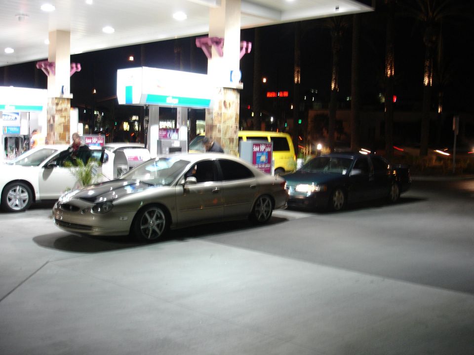 Gold sedan, possibly a Ford Taurus, at a gas station at night
