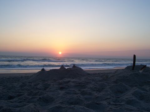 1994 Ford Probe - A tranquil beach scene unfolds with sandcastles in the foreground and the sun setting over the ocean.