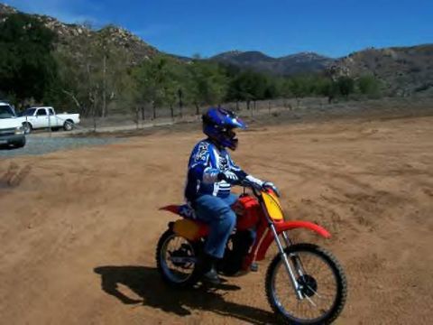 1972 Ford Ranchero - A dirt bike rider sits on a red motorcycle in a dusty outdoor area with hills and trees.