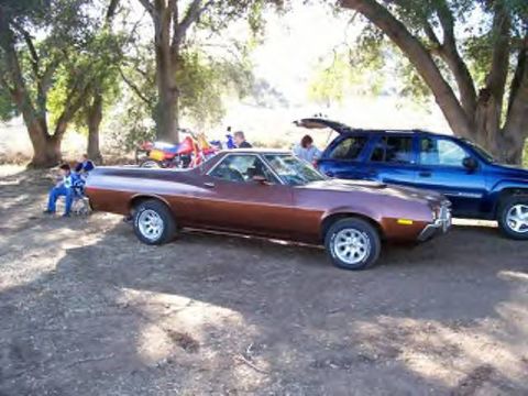 1972 Ford Ranchero - A brown 1972 Ford Ranchero is parked under trees, with a blue SUV and motorcycles visible in the background.