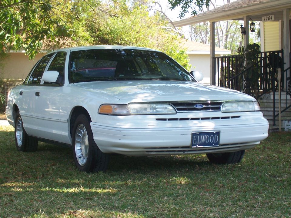 White Ford Crown Victoria parked on grass in front of a house