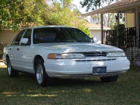 1997 Ford Crown Victoria - A white 1997 Ford Crown Victoria sedan is parked on a grassy lawn in front of a residential building.