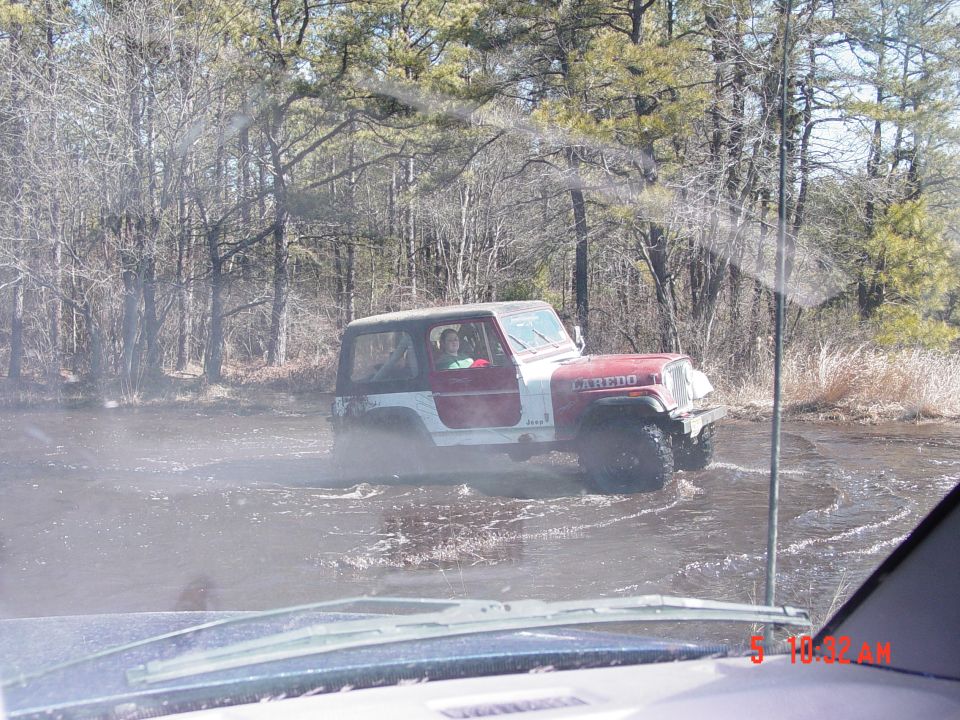 Red and white Jeep Wrangler Laredo driving through water