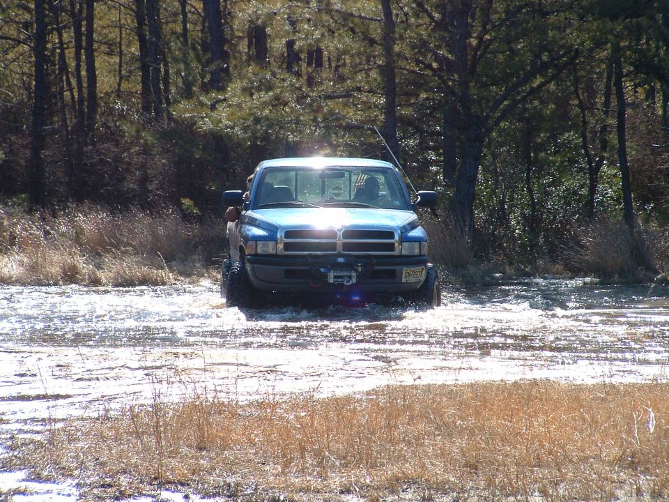 Blue Dodge Ram pickup with winch crossing a frozen flooded field, headlight glare on the water