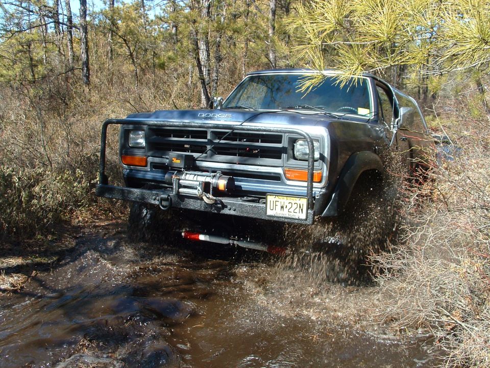 Front of a dark Dodge truck with brush guard and winch splashing through a muddy wooded trail