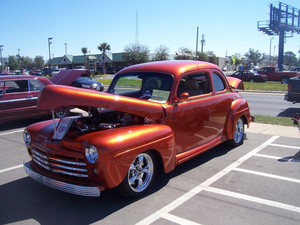 Candy orange late-1940s Ford coupe hot rod with hood open at a car show, front three-quarter view