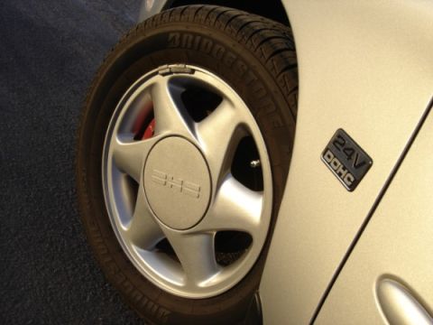1999 Ford Taurus - Close-up of a car's wheel and fender emblem, showing tire tread and a badge.