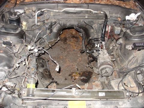 1986 Mazda RX-7 - The engine bay of a vehicle is shown, with the engine removed and various components and wiring exposed.
