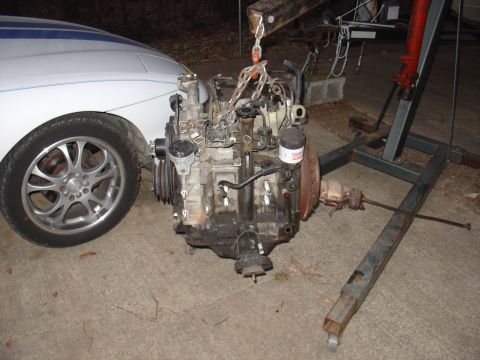 1986 Mazda RX-7 - Engine hoist lifting a rotary engine out of a car. The engine appears to be a Mazda rotary.