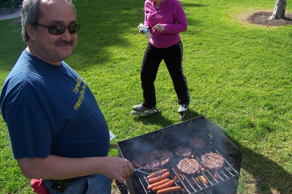 Man in blue t-shirt grilling hot dogs and hamburgers on a barbecue in a park