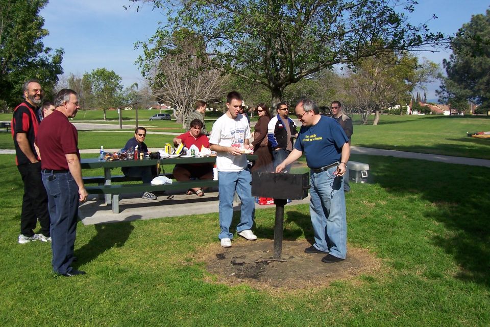 People gathered around a picnic table and barbecue grill in a park