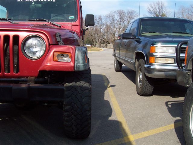 Front view of a red Jeep next to a dark green pickup truck. Text on the Jeep reads 'KCJeepClub.org'