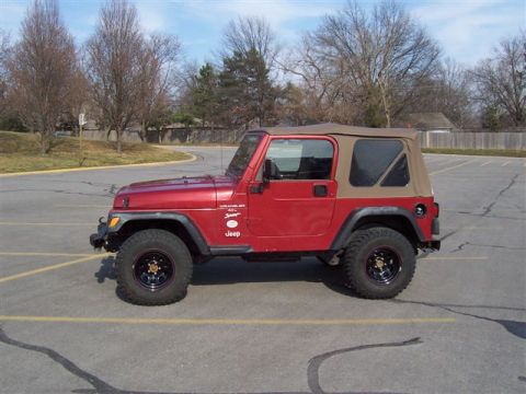 1998 Jeep TJ - A red 1998 Jeep TJ Wrangler is parked in a lot, showing its side profile and tan soft top.