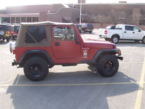 1998 Jeep TJ - Side view of a red 1998 Jeep TJ Wrangler Sport with a tan soft top and aftermarket black wheels.