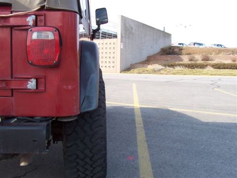 1998 Jeep TJ - The rear of a red Jeep Wrangler is shown, with a concrete wall and stairs in the background.
