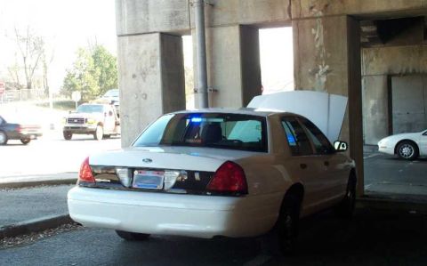 1998 Ford Crown Victoria - A white police car with its hood open is parked under a concrete structure, with another vehicle visible in the background.