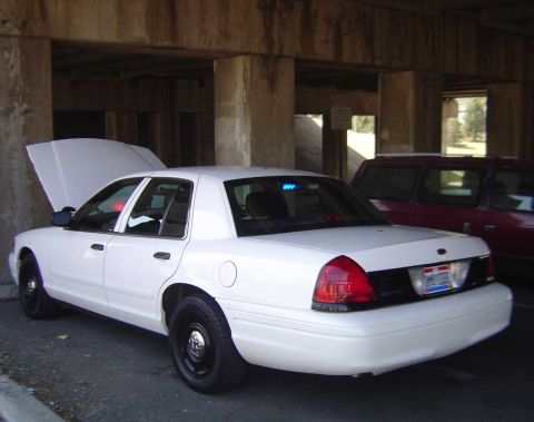 1998 Ford Crown Victoria - A white 1998 Ford Crown Victoria police car is parked with its hood open, under a concrete overpass, with another vehicle visible behind it.