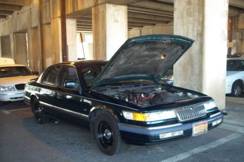 1998 Ford Crown Victoria - A dark sedan, likely a Mercury Grand Marquis, is parked with its hood open, revealing the engine compartment.