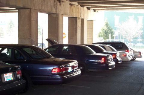 1998 Ford Crown Victoria - A line of sedans, likely police interceptors, are parked in a lot under a bridge.