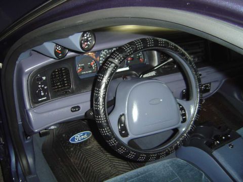 1998 Ford Crown Victoria - The dashboard of a car features aftermarket gauges and a Ford-branded floor mat.