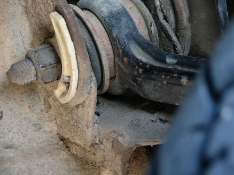 Close-up of muddy control arm bushing bolt with cracked plastic washer on truck front suspension