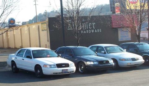1998 Ford Crown Victoria - Several police interceptor sedans are parked in front of a building with a sign that reads 'Ziemer Hardware'.