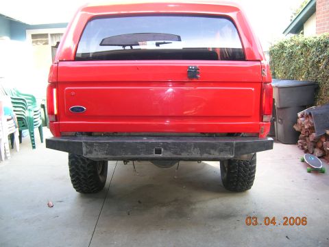 1985 Ford Bronco - The rear of a red Ford Bronco is shown with a black aftermarket bumper and a tow hitch receiver.