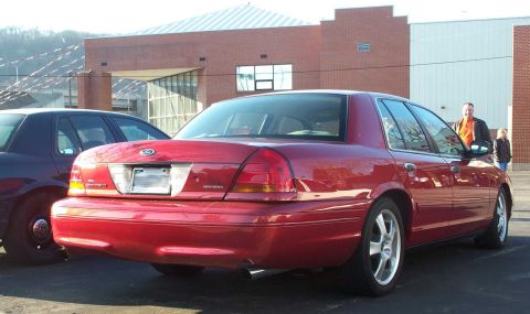 1998 Ford Crown Victoria - A red Ford Crown Victoria is parked next to a dark sedan, with a building in the background.