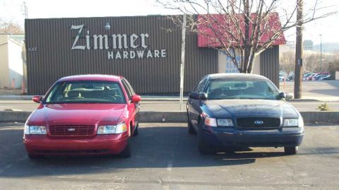 1998 Ford Crown Victoria - Two Ford Crown Victorias, one red and one blue, are parked in front of Zimmer Hardware.
