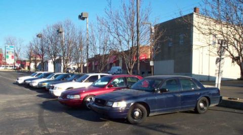 1998 Ford Crown Victoria - A row of Ford Crown Victoria Police Interceptors are parked in a lot on a sunny day. The vehicles are in various colors including blue, red…