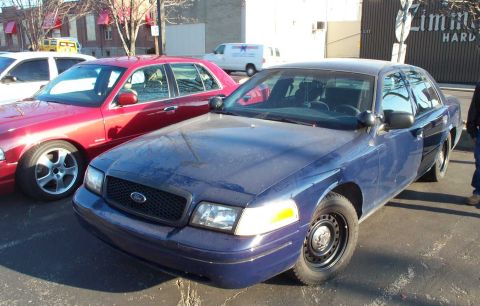 1998 Ford Crown Victoria - A blue 1998 Ford Crown Victoria is parked in a lot next to a red sedan.