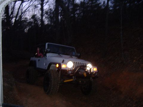 2004 Jeep Wrangler - A white Jeep Wrangler TJ navigates a dirt path at twilight, its headlights illuminating the trail ahead.